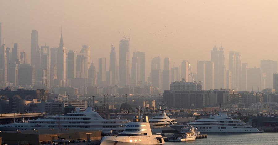 Dubai Marina with luxury yachts against a skyline of iconic skyscrapers in the morning light.