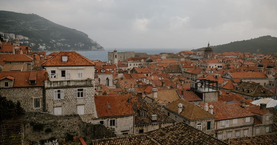Cityscape of residential houses with tiled roofs and brick walls on hills near calm ocean in overcast weather