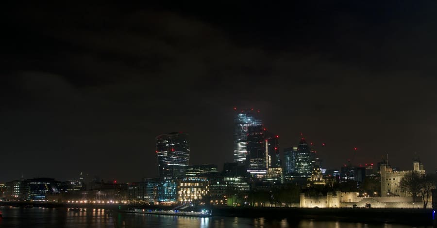 Dramatic night view of London's skyline featuring modern skyscrapers and the historical Tower of London.